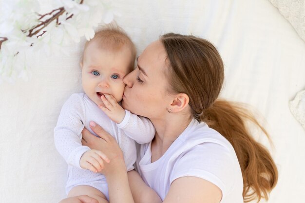 Portrait of a mother with a baby a mother kisses a child and gently hugs him on a white bed at home maternal love and care