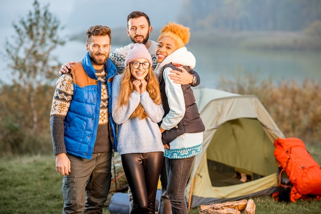 Portrait of multi ethnic group of friends dressed in sweaters hugging together and warming up at the camping during the evening