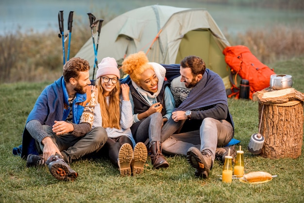 Portrait of multi ethnic group of friends dressed in sweaters hugging together and warming up at the camping during the evening