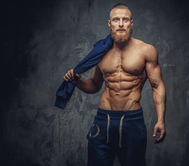 Portrait of muscular guy with beard in blue sports pants isolated on grey background.