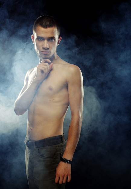 Portrait of a muscular male model against dark background with smoke.