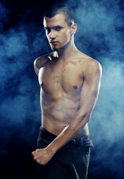 Portrait of a muscular male model against dark background with smoke