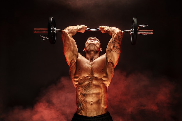 Portrait of muscular man lifting dumbbell in red smoke     Exercise for triceps  Motivation 