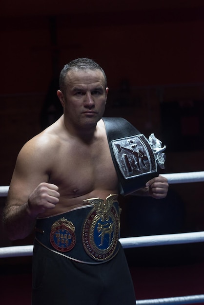 portrait of muscular professional kick boxer with his championship belt in the training ring