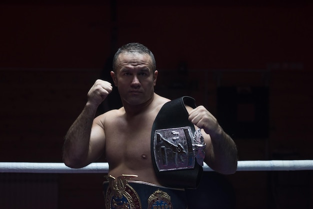 portrait of muscular professional kick boxer with his championship belt in the training ring