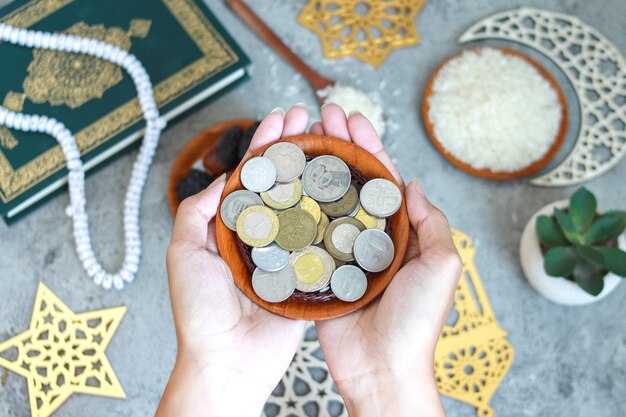 Photo portrait of muslim hands holding a bowl of coins with islamic decoration on the background top view