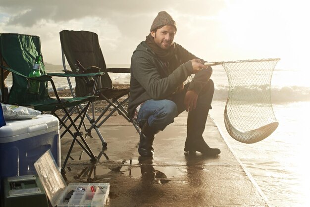 Photo portrait net and beach with man fish and hobby with equipment sunshine and weekend break person ocean and guy with tools for activity and happiness with waves shore and seaside with lens flare