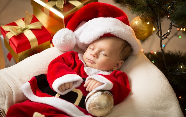 Portrait of newborn baby boy in Santa clothes lying under Christmas tree