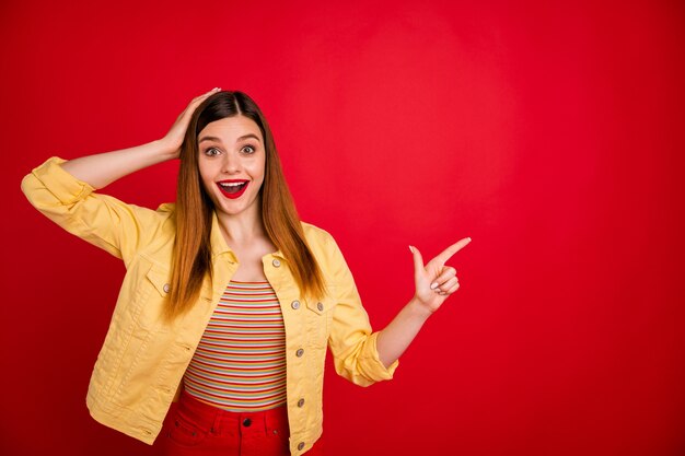 Portrait of  nice-looking attractive lovely lucky amazed glad cheerful cheery red-haired girl demonstrating copy space ad advert isolated on bright vivid shine vibrant red color background