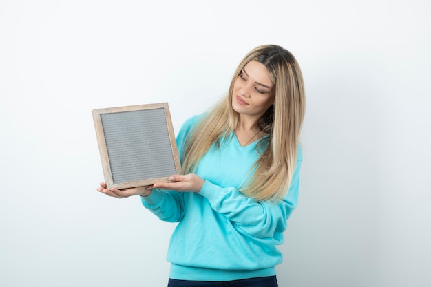 Portrait of nice-looking lady holding frame against white wall