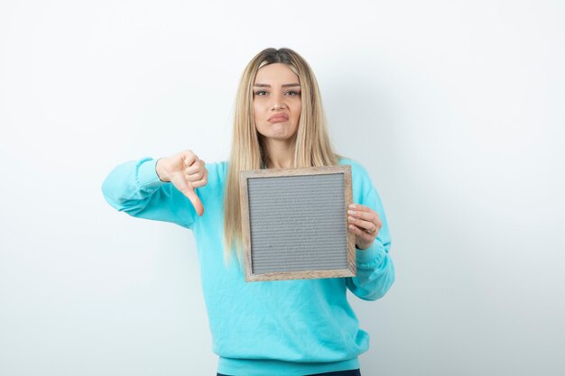 Portrait of nice-looking lady holding frame and showing thumb down