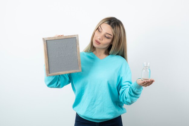 Portrait of nice-looking lady holding in hands frame and glass pitcher