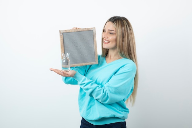 Portrait of nice-looking lady holding in hands frame and glass pitcher