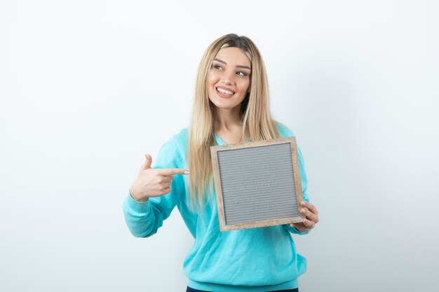 Portrait of nice-looking lady pointing at frame against white wall