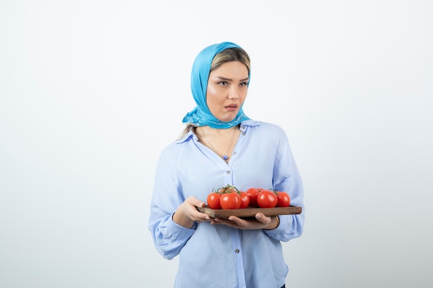 Portrait of nice woman in blue shawl holding wooden board of red tomatoes