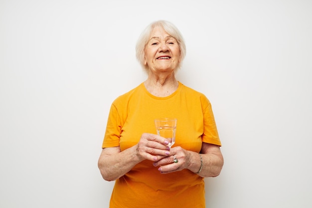 Portrait of an old friendly woman holding a glass of water health light background