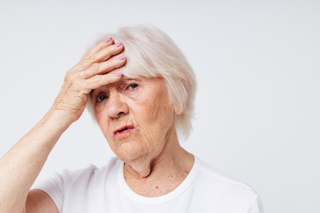 Portrait of an old friendly woman holding his head discontent problem light background