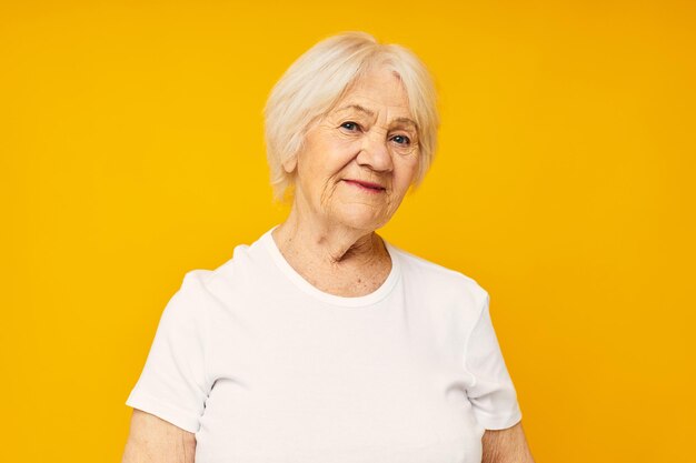 Portrait of an old friendly woman in white tshirt posing fun yellow background