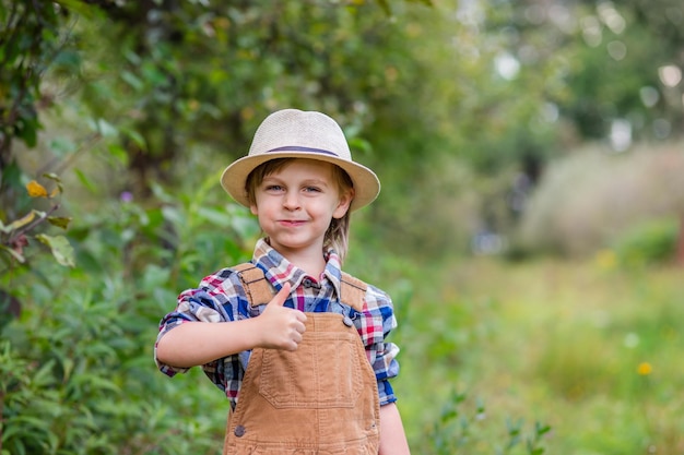 Portrait of one cute boy in a hat in garden with a red apple emotions happiness food Autumn harvest