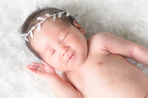 Portrait of a one month old sleeping, newborn baby girl. She is wearing a crown headband and sleeping on a white blanket. Concept portrait studio fashion newborn.