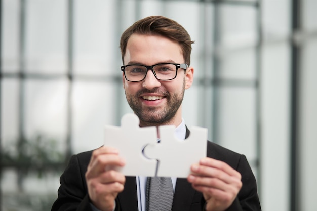 Portrait of optimistic bearded businessman holding puzzle pieces solving tasks looking at camera