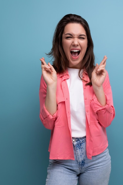 Portrait of optimistic brunette young woman in shirt and jeans with fingers crossed in hope