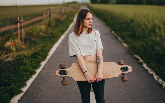 Portrait of an ordinary teen girl from the village the girl holds a longboard in a hand and smiles h