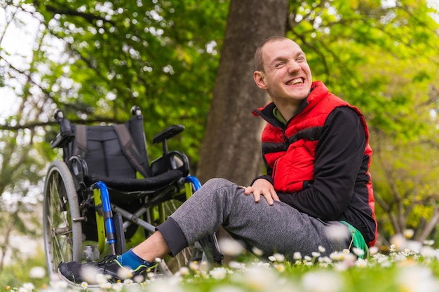 Portrait of a paralyzed young man sitting on the grass next to the wheelchair a daisy flowers smiling in nature