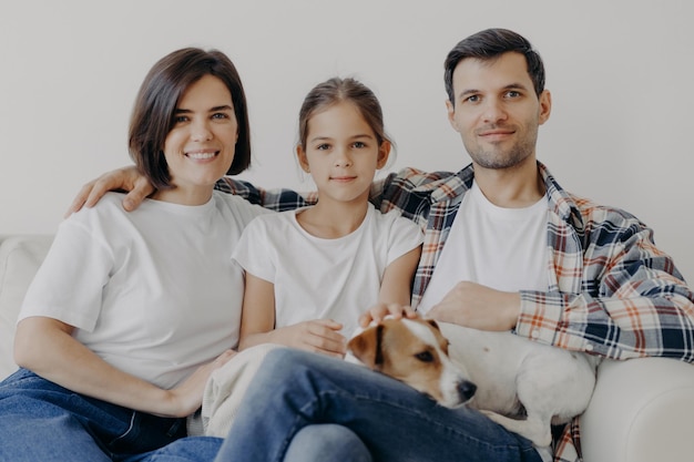 Photo portrait of parents with daughter and puppy sitting on sofa at home