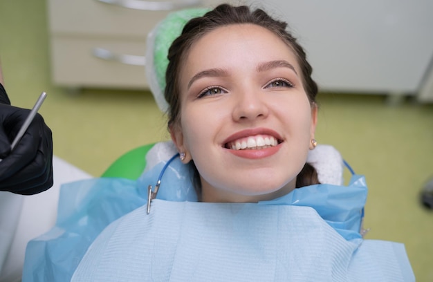 A portrait of a patient with white healthy teeth and a smile at the dentist's office she sits in a chair with a napkin on her chest