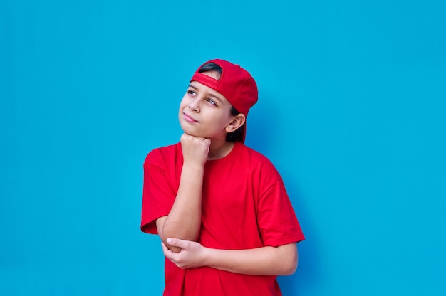 A Portrait of pensive boy in red cap and t-shirt with hand on face