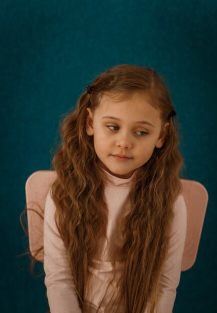 Portrait of a pensive little girl with long hair on a blue background