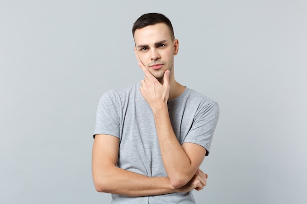 Portrait of pensive puzzled young man in casual clothes put hand prop up on chin 