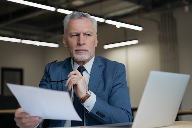 Portrait of pensive senior lawyer holding business documents