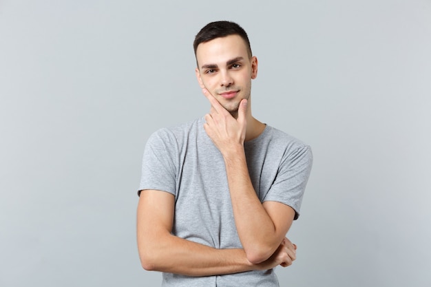 Portrait of pensive smiling young man in casual clothes put hand prop up on chin 