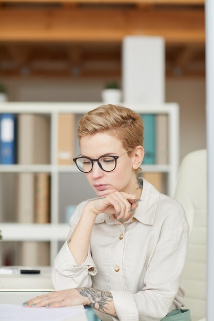 Portrait of pensive tattoed businesswoman working at desk in office