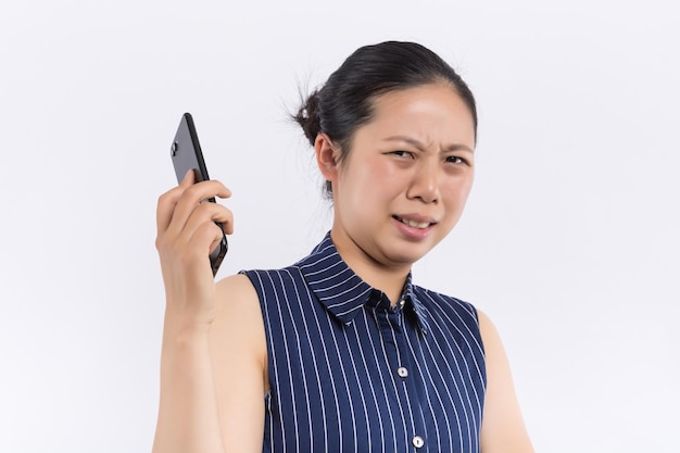 Portrait of a pensive young asian woman holding mobile phone and looking away with hand on her chin isolated over white background