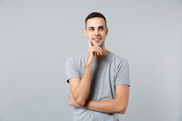 Portrait of pensive young man in casual clothes looking aside and put hand prop up on chin 