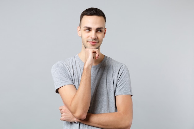 Portrait of pensive young man in casual clothes looking aside and put hand prop up on chin 