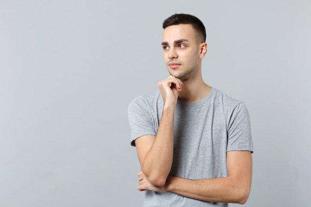 Portrait of pensive young man in casual clothes looking aside and put hand prop up on chin 