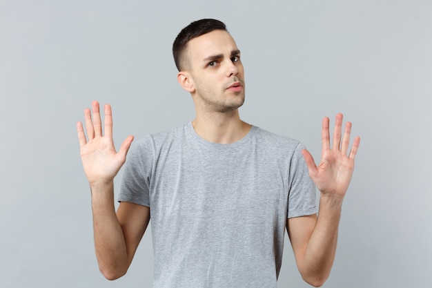 Portrait of perplexed young man in casual clothes, rising hands showing palms 