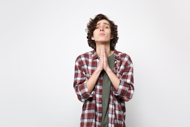 Photo portrait of pleading young man in casual clothes looking camera, folded his hands, praying isolated on white wall background in studio. people sincere emotions, lifestyle concept. mock up copy space.