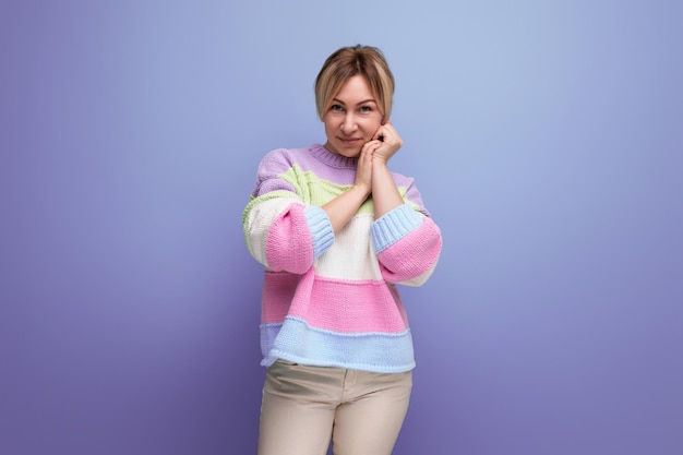 Portrait of pleasant shy blond young woman in casual outfit smiling on purple background with copy