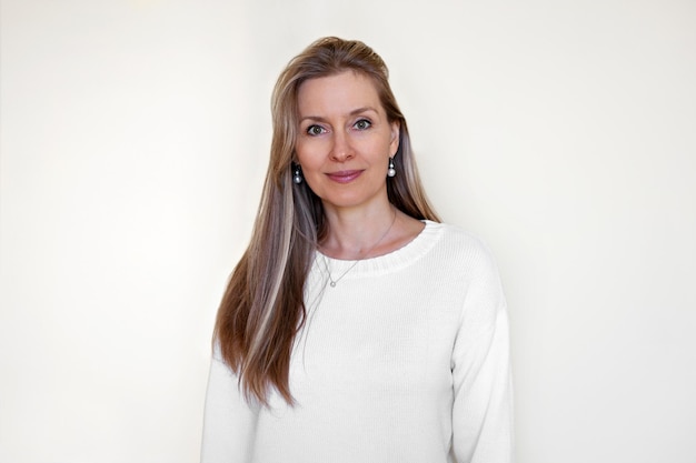 Portrait of pleased Caucasian woman with long hair, forty years old, looking into the camera, wearing white clothes, isolated on white background. Beautiful Model looks into the camera