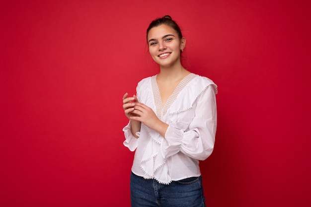 Portrait of positive cheerful fashionable woman in formalwear holding two hands together looking at camera isolated on red background with copy and empty space.