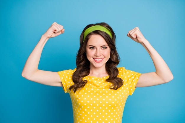 Photo portrait of positive cheerful girl show her hand muscles wear polka-dot clothes isolated over blue color background