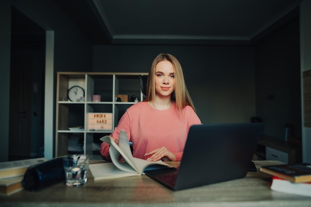 Portrait of a positive female student sitting at home at work with laptop books and notebook