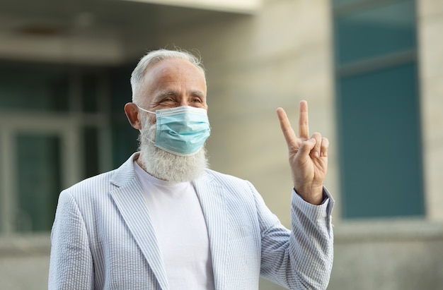 Portrait of positive handsome senior business man with medical mask smiling friendly and waving hand