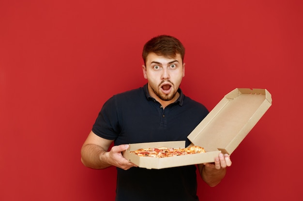 Portrait of positive man stands and opens box of delicious fresh pizza