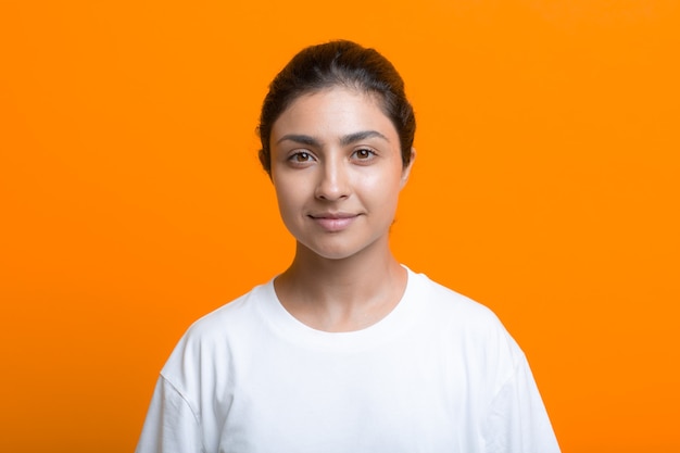 Portrait of positive smiling young adult indian woman in tshirt orange background